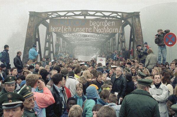 Люди на мосту на Штубенраухштрассе в ноябре 1989-го, где открылся еще один погранпереход между Восточным и Западным Берлином. На западной стороне лозунг: Мы приветствуем наших соседей. - Sputnik Беларусь