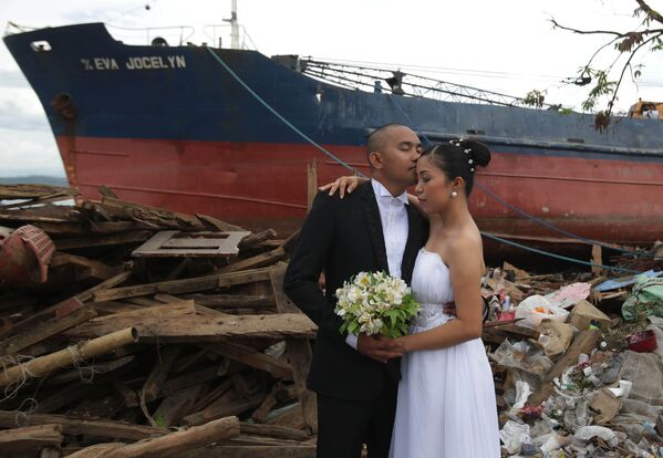 Жених Эрвин Нирва целует свою невесту Ризу на фоне разрушенных тайфуном домов и корабля на Филиппинах - Sputnik Беларусь