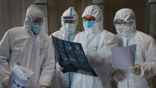 Медицинские работники в защитных костюмах осматривают снимок компьютерной томографии - Sputnik Беларусь