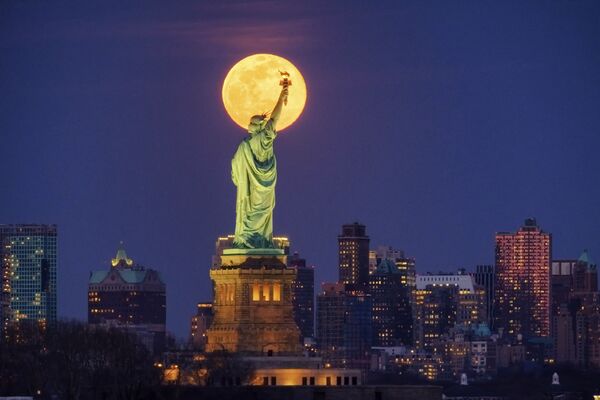 Восходящая полная луна проходит перед статуей Свободы вечером в понедельник, 9 марта 2020 года, в Нью-Йорке - Sputnik Беларусь