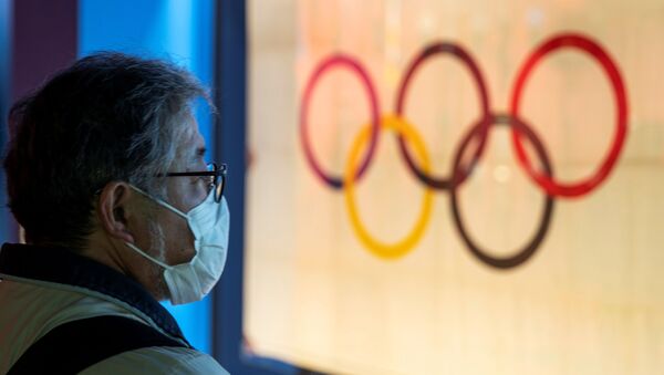 Мужчина в защитной маске стоит перед Олимпийским флагом в Токио  - Sputnik Беларусь