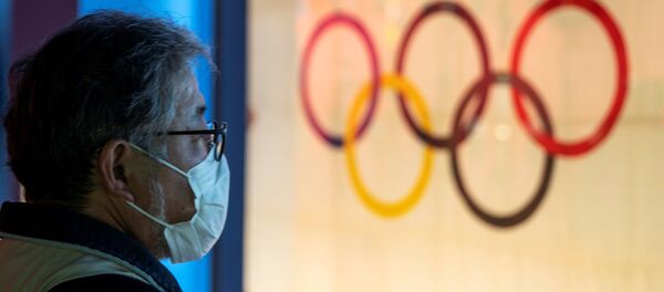 Мужчина в защитной маске стоит перед Олимпийским флагом в Токио  - Sputnik Беларусь