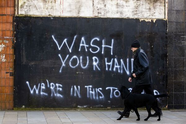 Мужчина с собакой напротив граффити с призывом мыть руки в Северной Ирландии - Sputnik Беларусь