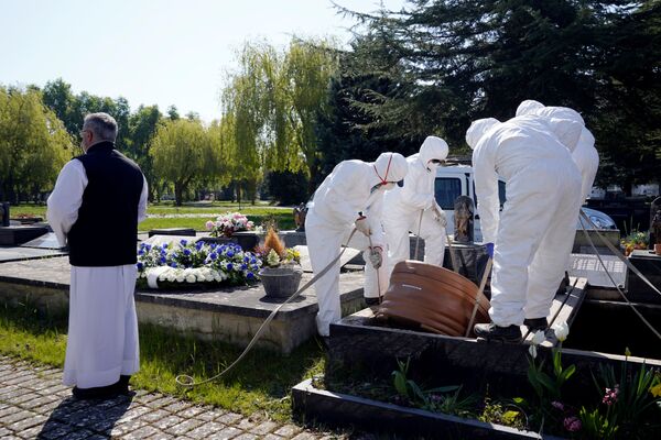 Муниципальные работники в защитном снаряжении опускают гроб на кладбище в Витории, Испания - Sputnik Беларусь