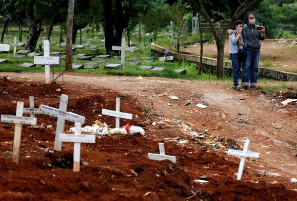 Родственники в масках стоят рядом с могилами жертв COVID-19 на кладбище в Джакарте, Индонезия - Sputnik Беларусь
