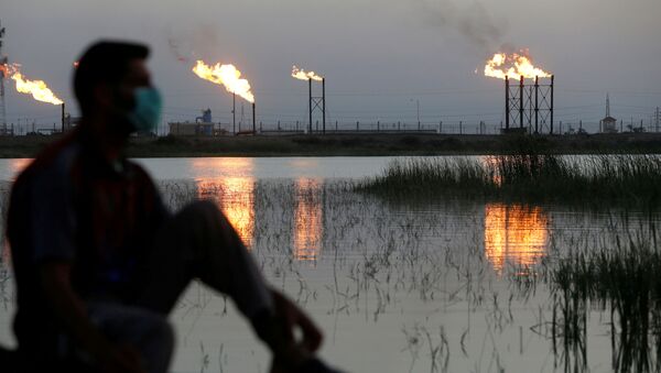 Мужчина в маске смотрит на пламя из факельных труб на нефтяном месторождении Нахр Бин Умар к северу от Басры, Ирак - Sputnik Беларусь