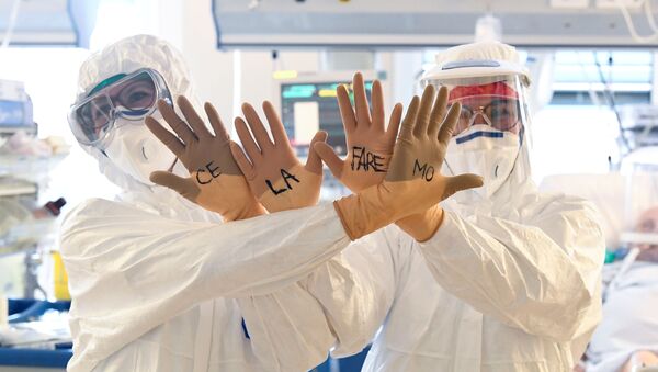 Медицинские работники в защитных костюмах показывают свои руки с надписью на перчатках Ce la faremo (Мы сделаем это) - Sputnik Беларусь