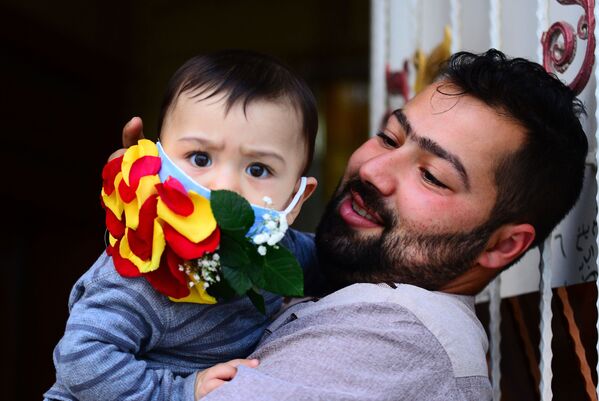 Мужчина с ребенком в украшенной цветами защитной маске в Эн-Наджафе, Ирак - Sputnik Беларусь