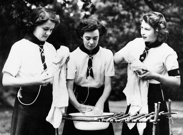 Принцесса Елизавета (справа) помогает мыть посуду после трапезы на свежем воздухе, которую она помогла приготовить во время посещения лагеря девушек-гайдов в Англии 29 июля 1944 года.  - Sputnik Беларусь