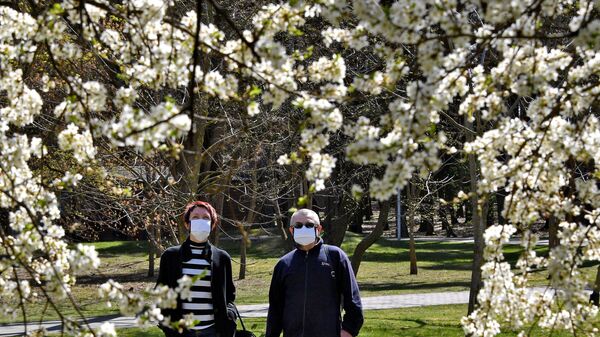 Мужчина и женщина в защитных масках возле цветущего дерева в парке Челюскинцев в Минске - Sputnik Беларусь