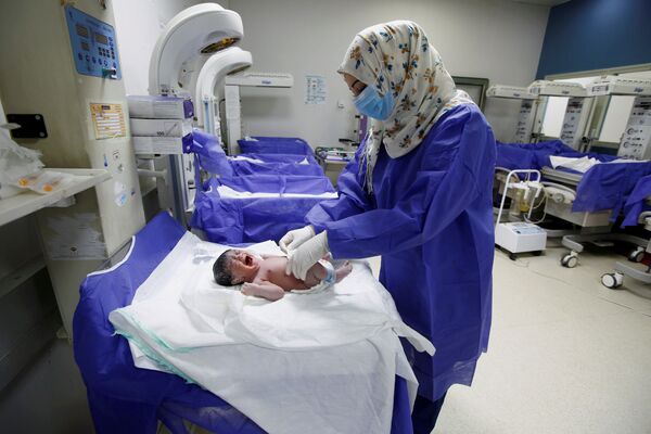 Медсестра в защитной маске и перчатках ухаживает за новорожденным в роддоме в Наджафе, Ирак - Sputnik Беларусь