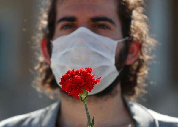 Член профсоюзного коммунистического движения в защитной маске держит гвоздику во время празднования Первого мая в Афинах - Sputnik Беларусь