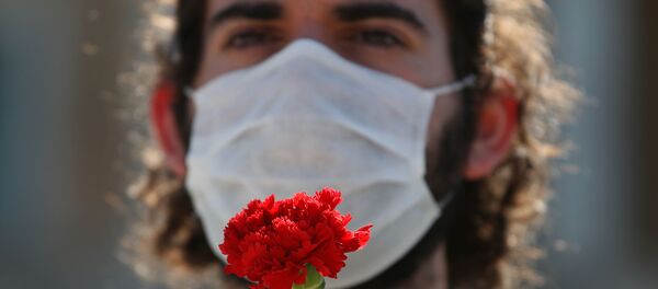 Член профсоюзного коммунистического движения в защитной маске держит гвоздику во время празднования Первого мая в Афинах - Sputnik Беларусь