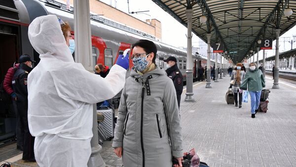 Супрацоўнік медыцынскай службы вымярае тэмпературу пасажыру бескантактным тэрмометрам на тэрыторыі вакзалу ў Маскве - Sputnik Беларусь